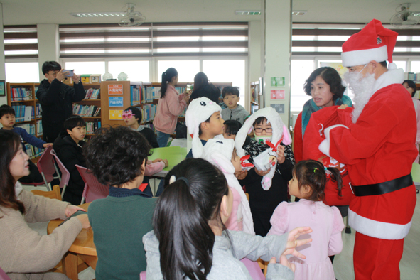 오갑초 다모임활동으로 산타복장을 한 윤덕진 교장이 어린이들에게 선물을 나눠주고 있다.