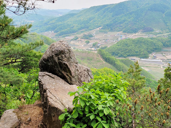 ▲국사산(봉) 정상 서쪽에 있는 전망바위와 그 뒤로 충도2리 마을 모습.